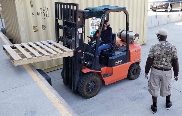 A woman operates a fork lift as a man watches
